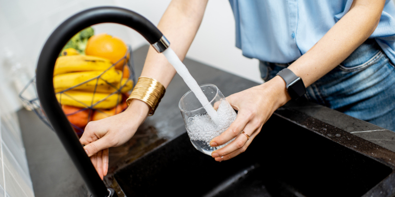 Woman filling glass with tap water for drinking on the kitchen